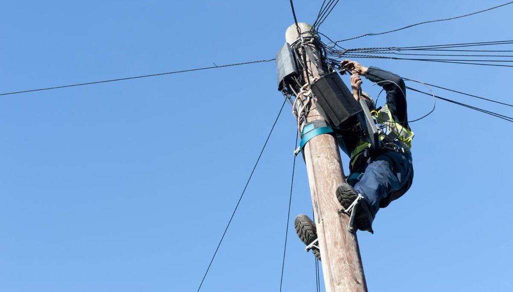 Man installing telephone and broadband cables on a telgraph pole.