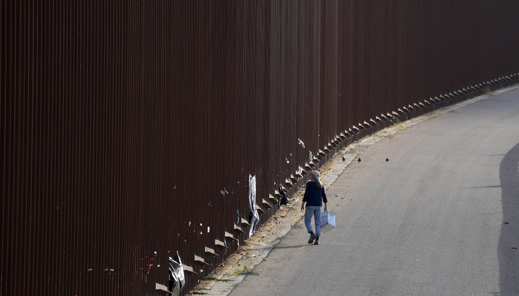 A volunteer walks along a border wall as she passes out baby wipes to migrants waiting to apply for asylum between two border walls, May 11, 2023, in San Diego. (AP)