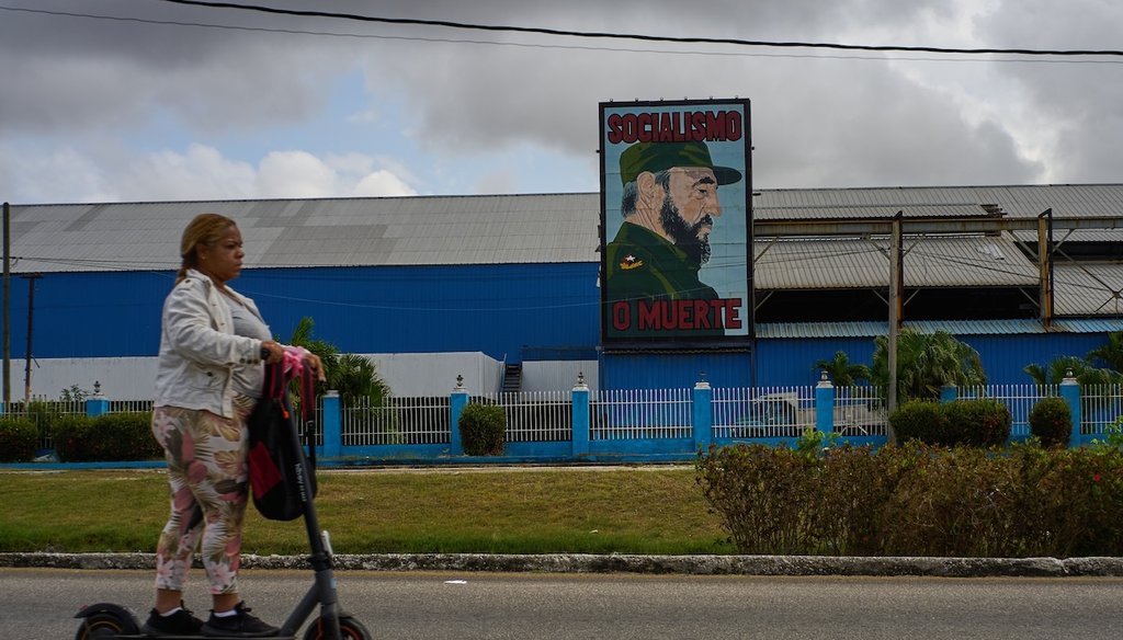A woman rides an electric scooter past an image of the late Cuban leader Fidel Castro, with the caption "Socialism or Death", in Havana, Cuba, on March 19, 2026. (AP)