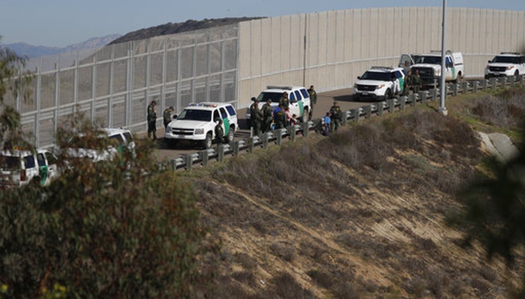 A woman and children stand amidst U.S. Border Patrol agents after crossing illegally over the border wall into San Diego, California, as seen from Tijuana, Mexico, Sunday, Dec. 9, 2018. (AP Photo/Rebecca Blackwell)