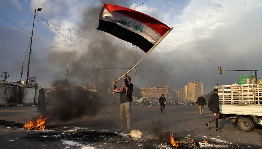 A protester waves the national flag while demonstrators set fire to close streets near Tahrir Square during a demonstration against the Iranian missile strike in Baghdad, Iraq on Jan. 8, 2020. (AP)