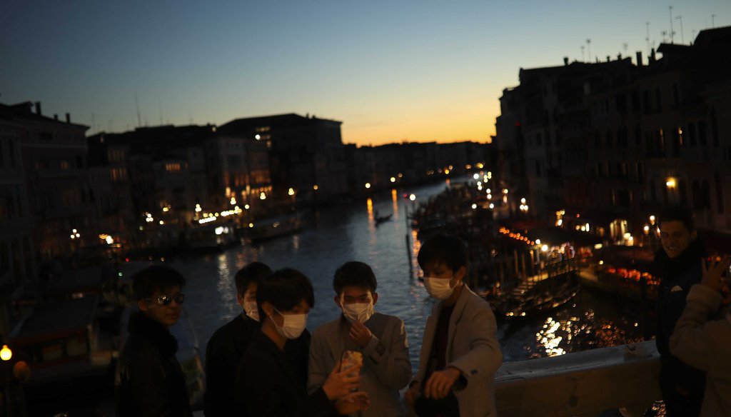 Tourists wearing protective masks pose for a photograph at the Rialto bridge as the sun sets in Venice, Italy, on Feb. 28, 2020. (AP)
