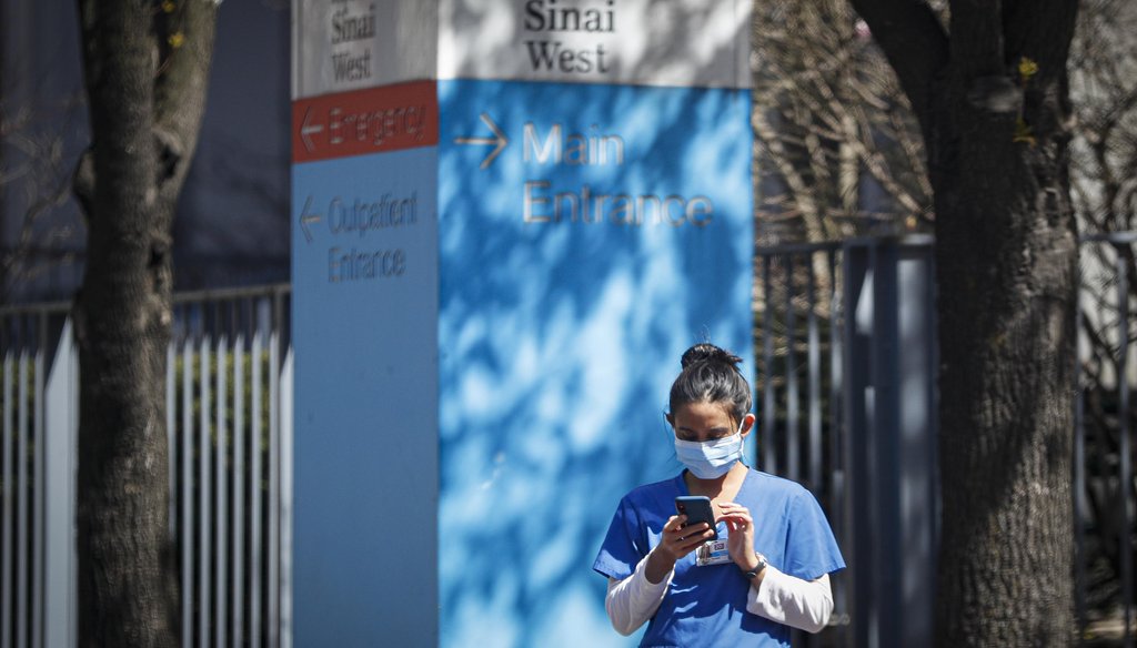A medical worker uses her phone while wearing a surgical mask outside Mt. Sinai West on March 26, 2020, in New York. (AP)