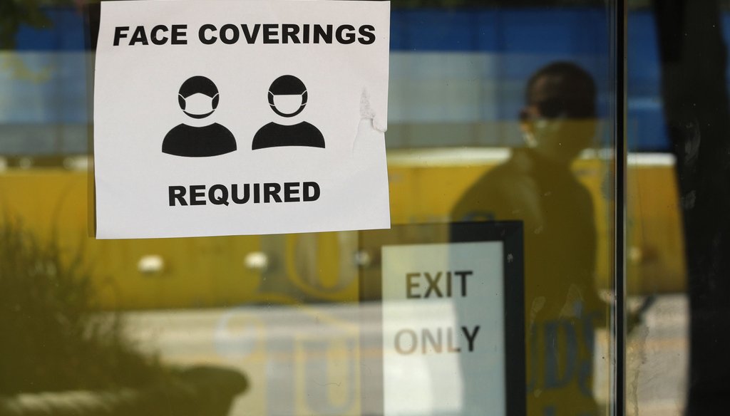 A man wearing mask to protect against the spread of COVID-19 is reflected next to a sign requiring face coverings at a business in San Antonio on June 24, 2020. (AP)