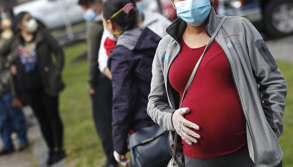 In this  May 7, 2020 photo, a pregnant woman wearing a face mask and gloves holds her belly as she waits in line for groceries during a food pantry sponsored by Healthy Waltham during the COVID-19 outbreak in Waltham, Mass. (AP)
