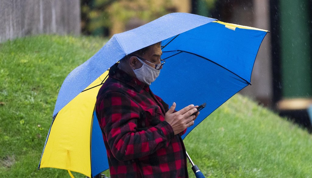 A man wears a mask to help prevent the spread of the coronavirus while using his phone on a rainy day. (AP)