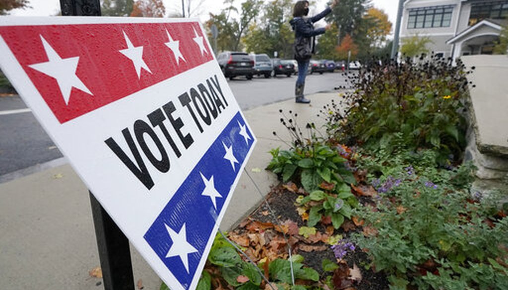 A passers-by uses a mobile device near a vote today sign outside a polling place during early in-person general election voting, Oct. 28, 2020, Wellesley, Mass. (AP)