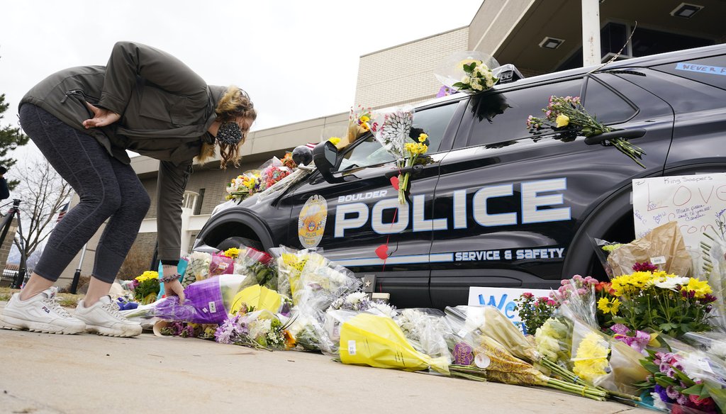 A woman leaves a bouquet of flowers next to a police cruiser parked outside the Boulder Police Department after an officer was one of the victims of a mass shooting at a King Soopers grocery store Tuesday, March 23, 2021, in Boulder, Colo.  (AP Images)