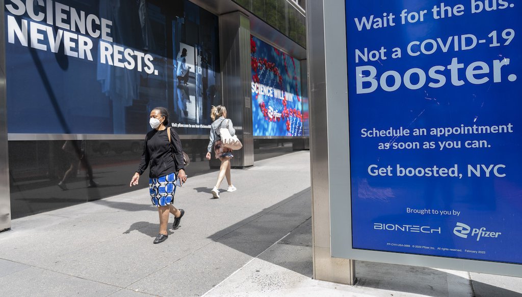 Pedestrians walk past a signs hanging outside Pfizer headquarters in New York and one hanging at a bus stop encouraging the Covid-19 booster, May 23, 2022. (AP)