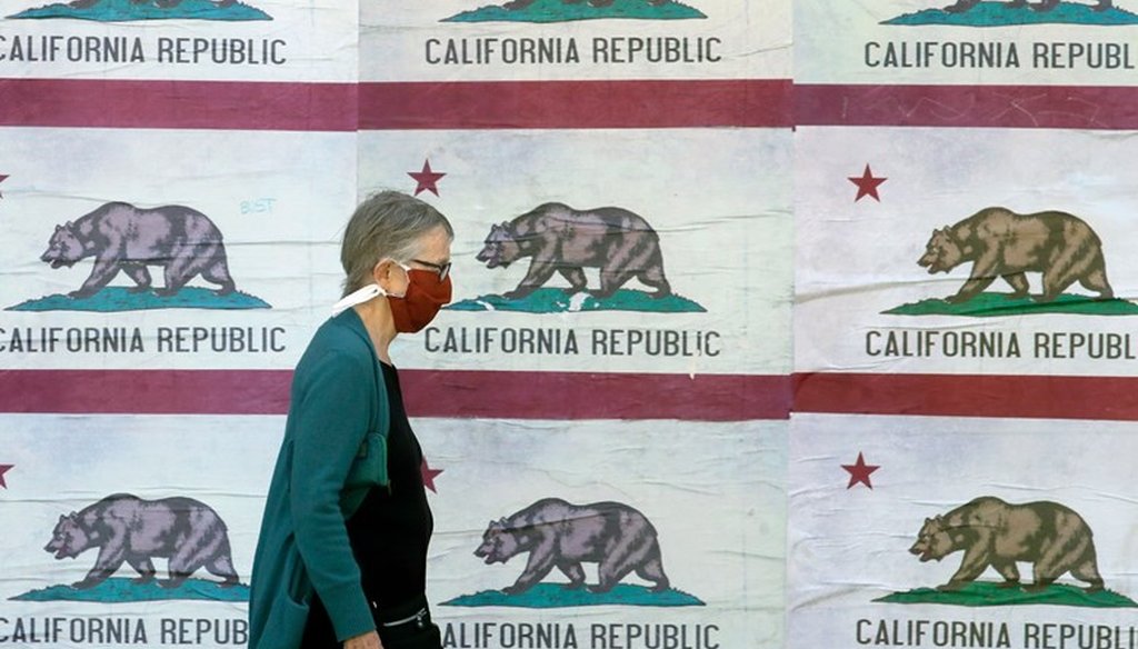 A pedestrian wearing a mask walks in front of a billboard displaying California flags in San Francisco, April 30, 2020, during the coronavirus outbreak. AP Photo/Jeff Chiu