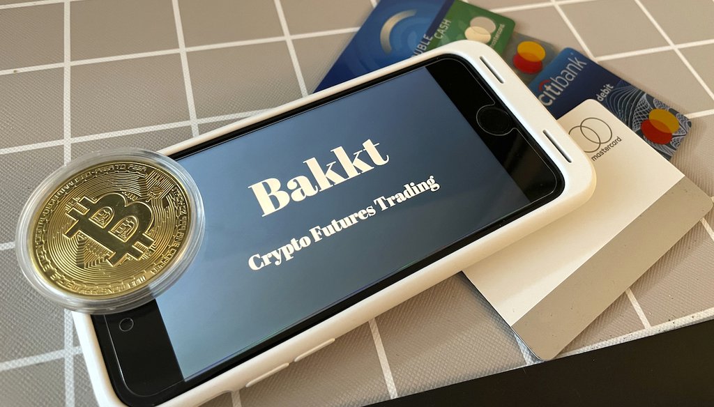 A physical rendering of a Bitcoin sits atop an iPhone showing crypto futures trading. Oct. 26, 2021 (AP)