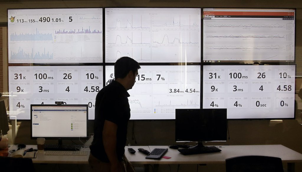 In this 2015 photo, an employee in the of DraftKings, a daily fantasy sports company, walks past screens displaying the company's online system stats in Boston. (Associated Press)