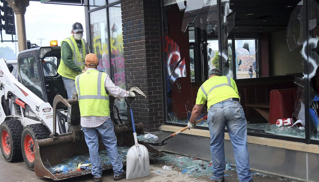 Workers clear broken glasses in front of a building near the Minneapolis Police Third Precinct after a night of rioting as protests continue over the arrest of George Floyd who died in police custody. (AP Photo/Jim Mone)