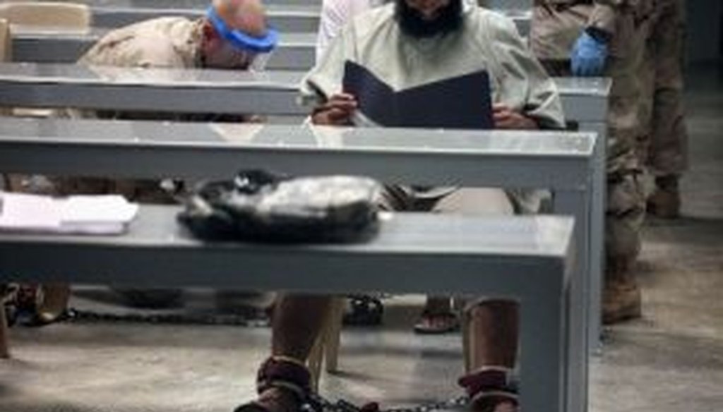 This 2010 photograph, made through one-way glass and reviewed by the U.S. military, shows a shackled Guantanamo detainee reading his materials in a "Life Skills" class as guards behind him shackle another detainee to the floor after bringing him to class.