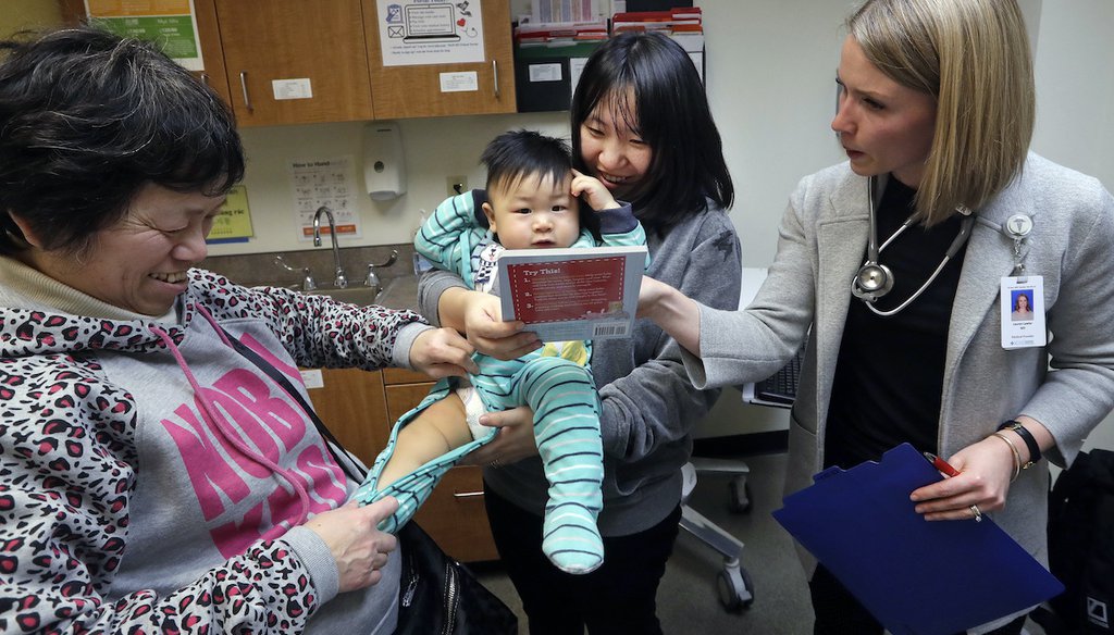 Held by his mother Wenyi Zhang, one-year-old Abel Zhang looks at a book with Dr. Lauren Lawler, right, as his grandmother Ding Hong helps him, moments after the child received a vaccine for measles, mumps, and rubella, Feb. 13, 2019, in Seattle. (AP)