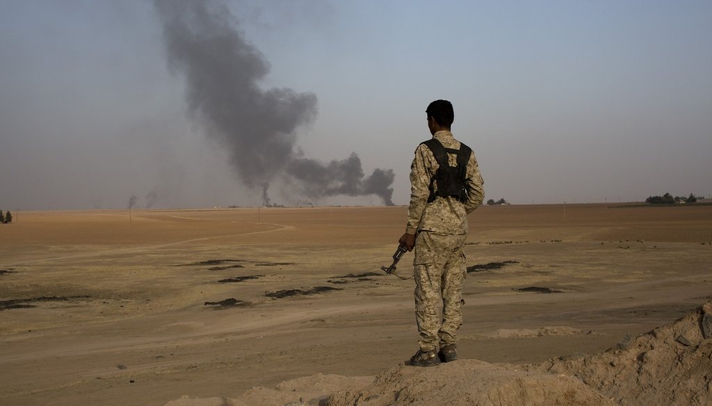 A member of an Arab tribal militia fighting the Islamic State watches as smoke rises from a crude oil refinery in Tel al-ail, Syria on Oct. 24, 2015 (New York Times). 
