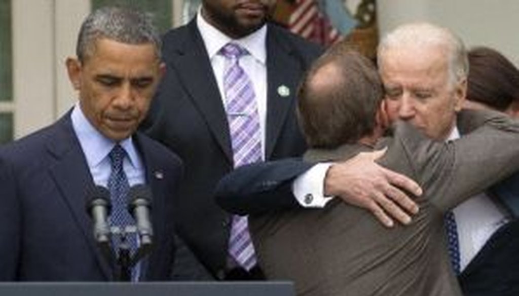 President Barack Obama stands at the podium as Mark Barden, father of a Newtown shooting victim, is embraced by Vice President Joe Biden during a Rose Garden news conference on gun policy.