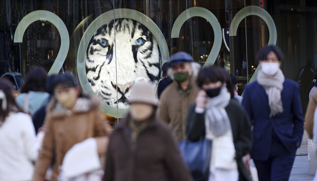 People wearing masks walk along a pedestrian crossing Tuesday, Jan. 18, 2022, in Tokyo. The Japanese government is placing Tokyo and a dozen other areas under a near-emergency status for COVID-19 as omicron cases surge.