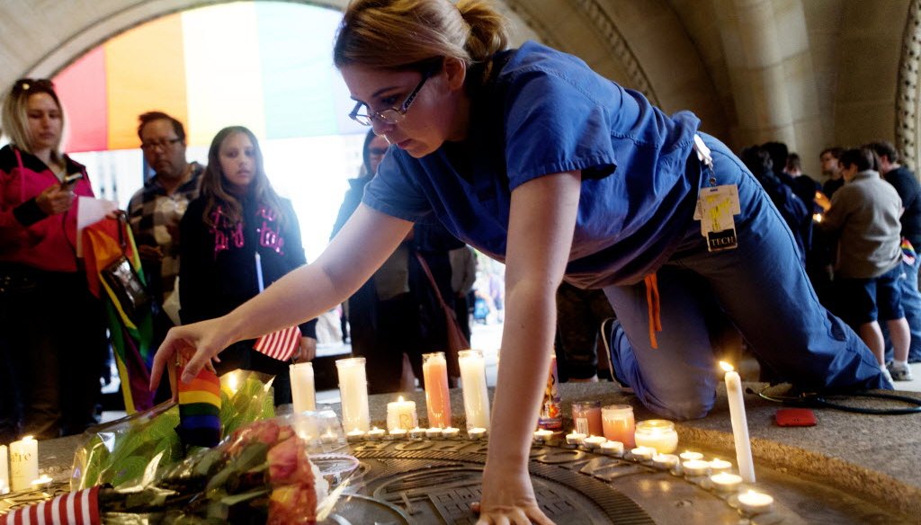 A woman places an LGBTQ flag in the middle of a circle of candles and roses during a vigil held for victims of the Orlando mass shooting at Milwaukee City Hall on June 13, 2016. (Calvin Mattheis photo)