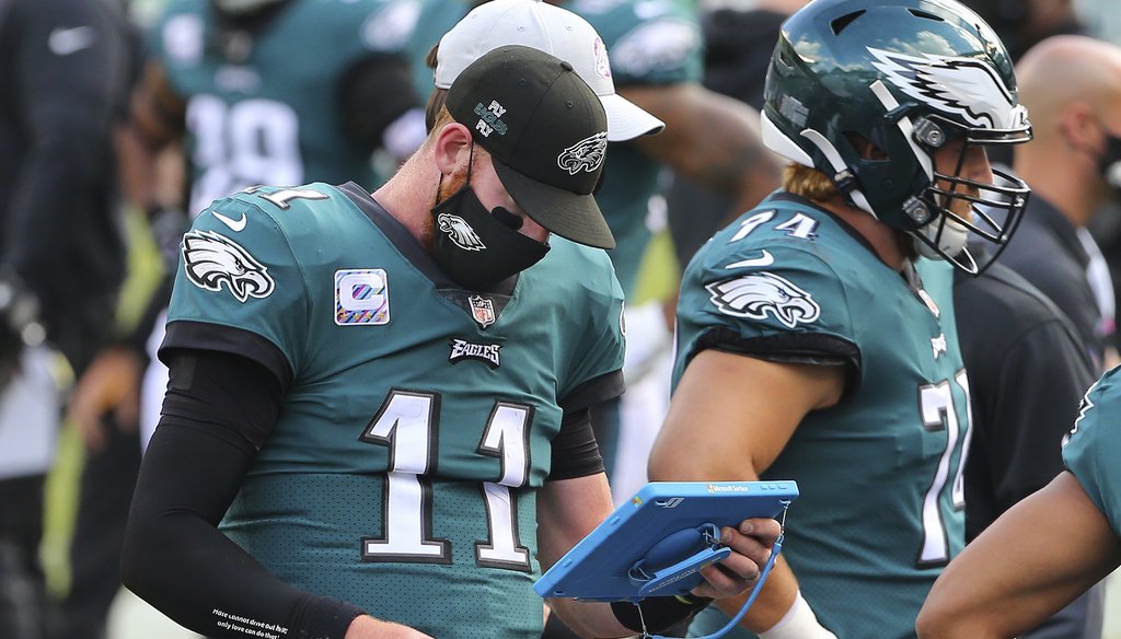 Philadelphia Eagles' Carson Wentz wears a mask as he looks at his Microsoft tablet during an NFL football game, against the Baltimore Ravens, Sunday, Oct. 18, 2020, in Philadelphia. (AP Photo/Rich Schultz)