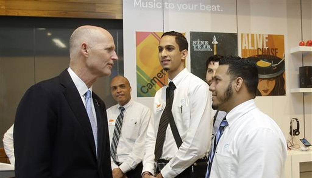 Gov. Rick Scott, left, talks to recently hired store employees Giancarlo Colon, right, and Demetrio Gomez, second from right, during the opening of a new AT&T store, Wednesday, Oct. 30, 2013, in Miami. (AP)