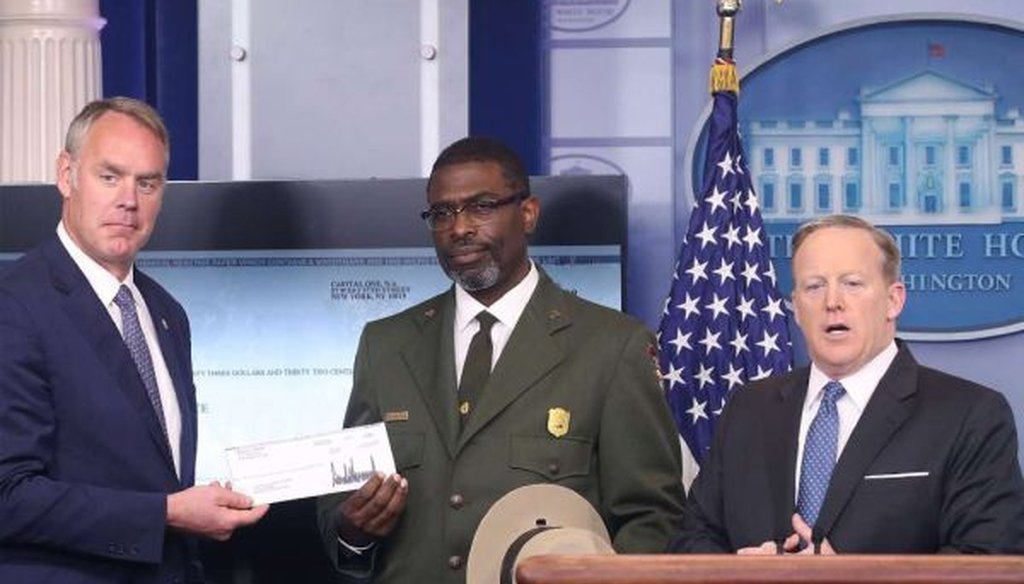 White House press secretary Sean Spicer (right) gives Interior Secretary Ryan Zinke (left) the first-quarter earnings of President Donald Trump as Harpers Ferry National Historical Park Superindendent Tyrone Brandyburg looks on. (Mark Wilson/Getty Images)