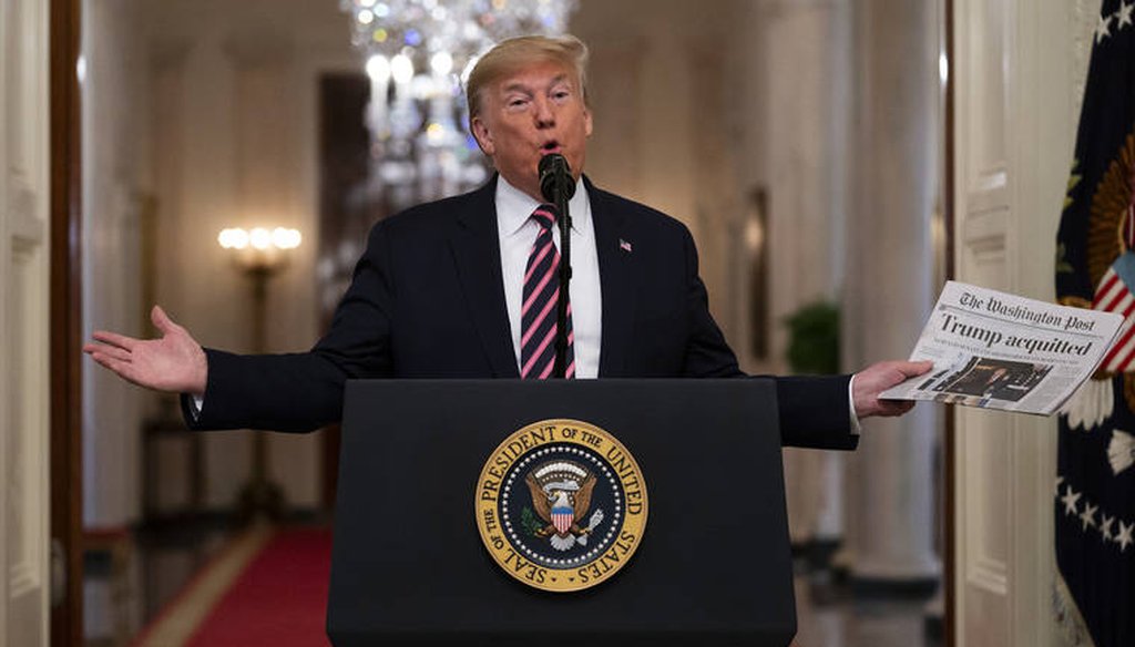 President Donald Trump holds up a newspaper with a headline that reads "Trump acquitted" as he speaks in the East Room of the White House, Thursday, Feb. 6, 2020, in Washington. (AP Photo/Evan Vucci)
