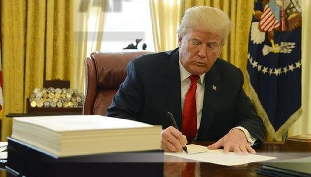 President Donald Trump signs a tax bill, stacked on his desk, in the Oval Office on Dec. 22, 2017. (Mike Theiler/Pool via CNP)