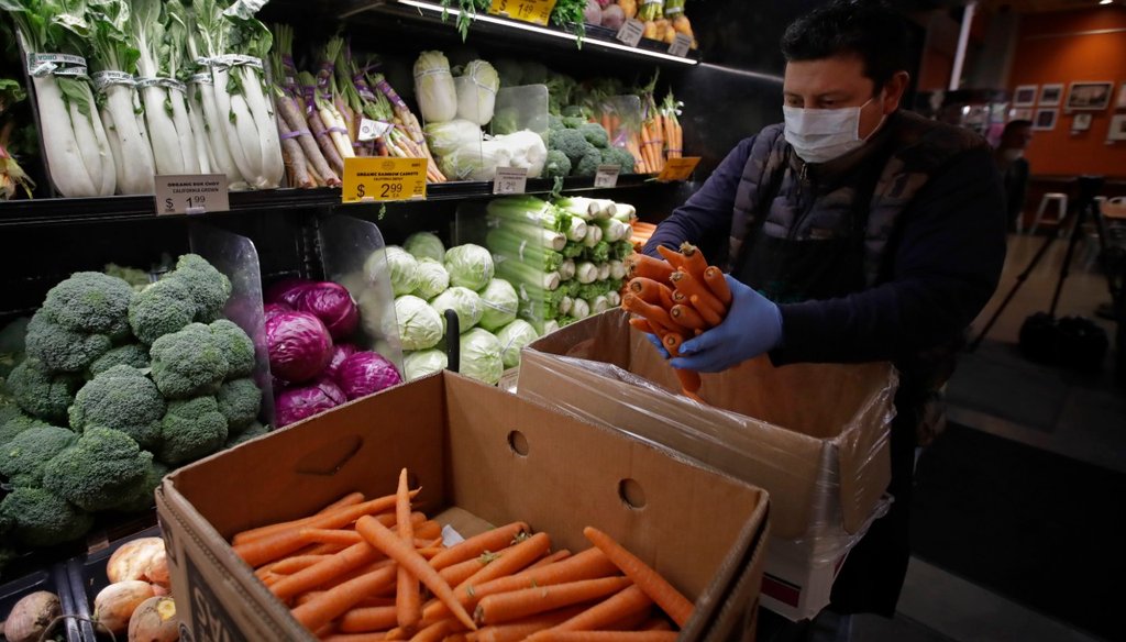 In this March 27, 2020, file photo, a worker, wearing a protective mask against the coronavirus, stocks produce before the opening of Gus's Community Market in San Francisco. (AP Photo/Ben Margot, File)