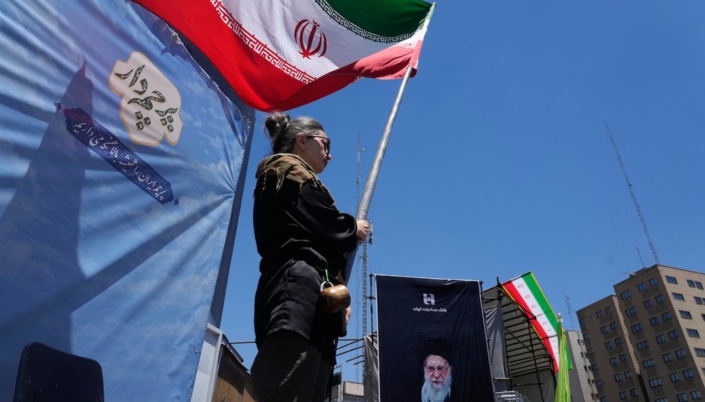 A woman waves an Iranian flag during a pro-government campaign as a portrait of the slain Supreme Leader Ayatollah Ali Khamenei is displayed at right, in downtown Tehran, Iran, June 15, 2026. (AP)
