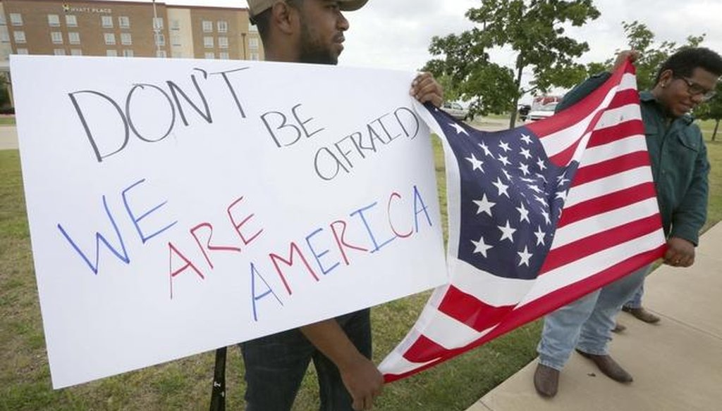 Joseph Offutt, left, and Raheem Peters hold a sign and U.S. flag near the site of the Garland, Texas, shooting of a cartoon contest event of the Muslim prophet Muhammad. (AP)