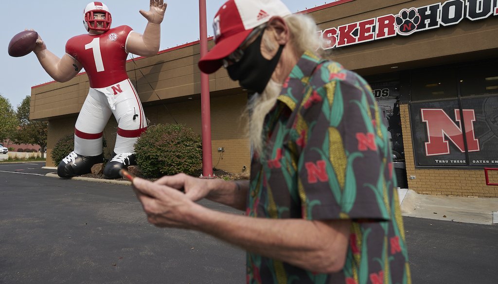A fan stops to take a picture of a giant inflatable football player standing in front of the Husker Hounds sports apparel store in Omaha, Neb. Omaha has a mask mandate, but the state as a whole doesn’t. (AP Photo/Nati Harnik)