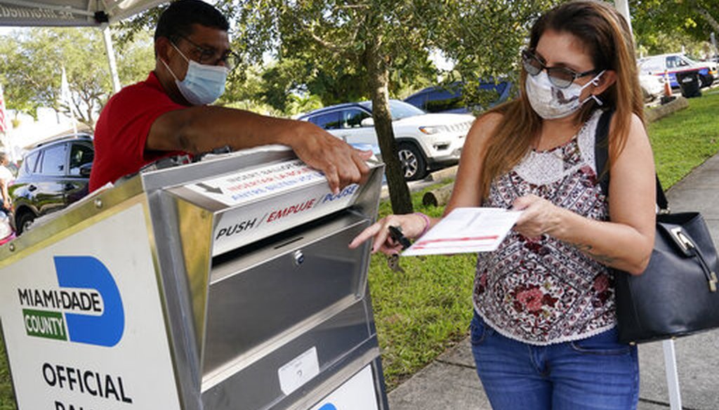 Carlos Amado, left, with the Miami-Dade Supervisor of Elections, guides Isabel Lui to the slot to drop off her ballot, Friday, Oct. 30, 2020 in North Miami, Fla. (AP)