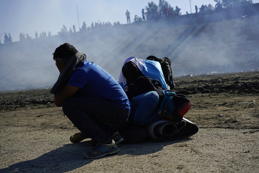 Three Honduran migrants huddle in the riverbank amid tear gas fired by U.S. agents on the Mexico-U.S. border. Nov. 25, 2018. (AP Photo/Ramon Espinosa)