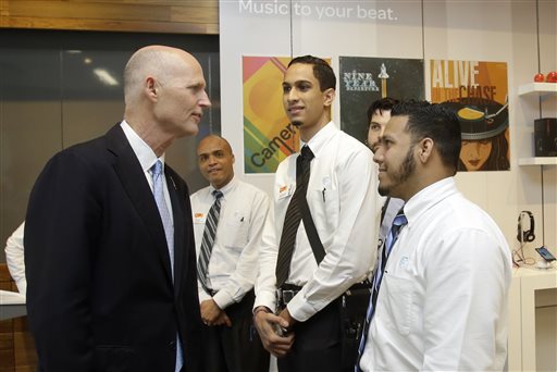 Gov. Rick Scott, left, talks to recently hired store employees Giancarlo Colon, right, and Demetrio Gomez, second from right, during the opening of a new AT&T store, Wednesday, Oct. 30, 2013, in Miami. (AP)