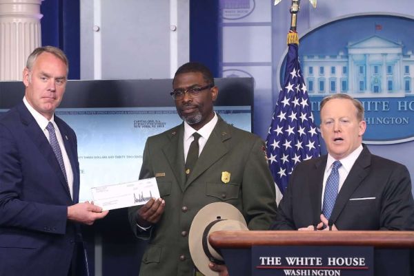 White House press secretary Sean Spicer (right) gives Interior Secretary Ryan Zinke (left) the first-quarter earnings of President Donald Trump as Harpers Ferry National Historical Park Superindendent Tyrone Brandyburg looks on. (Mark Wilson/Getty Images)